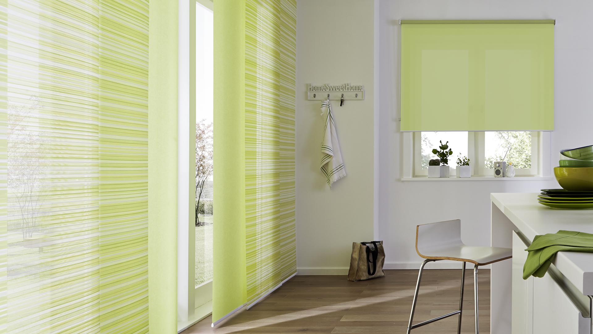 Grüne Flächenvorhänge mit einem eleganten Muster an Fenstern. Sichtbar in Kombination mit einem gleichfarbigen Rollo.